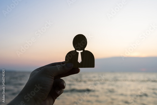 Businessman symbol raised against a sunset sea background. Concept of work stress, corporate employee relaxation, work relaxation, life happiness.
