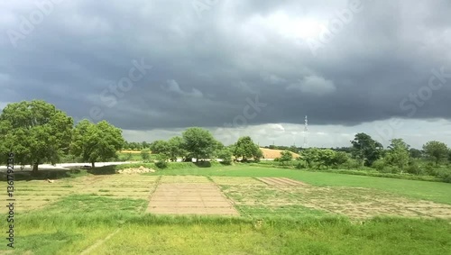A picturesque rural landscape showcases greenery, trees, and dramatic clouds over agricultural fields