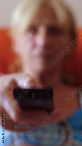 Vertical: A woman sitting on the couch zapping through TV channels. Focus on the remote control and the TV screen