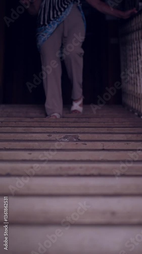 Vertical. A woman's legs are seen descending a long staircase inside a building, capturing the motion and elegance of each step. A dynamic interior scene.