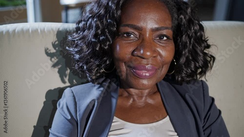 elderly black woman smiles in Sunday best, sitting on sofa, listening to conversation at a family event