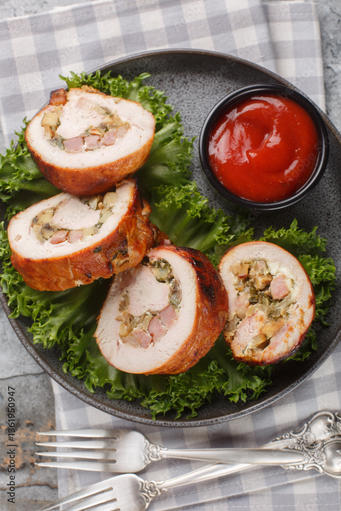 Turkey roll stuffed with bacon, onions and mushrooms served with tomato sauce close-up in a plate on the table. Vertical top view from above