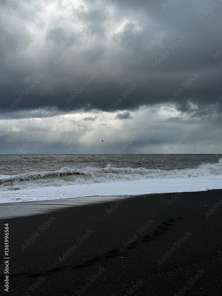 Black sand beach with footprints under a stormy sky