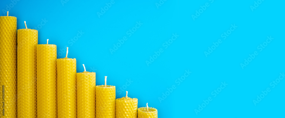 Fototapeta premium Descending yellow beeswax candles on blue background symbolize declining crypto market trends, price drop, weakening investor confidence, resembling financial graph movement.