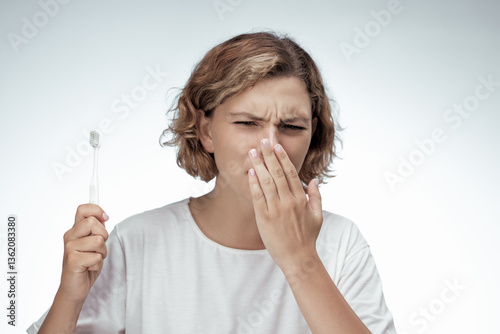 Cuadro en lienzo A woman in a white t-shirt covers her mouth and holds a toothbrush, showing signs of discomfort