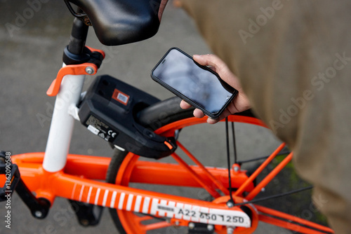 Man using mobile phone to unlock two-wheeled bike-sharing vehicle in city