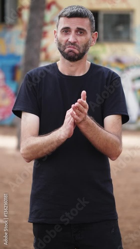 Vertical: A young man in a black shirt claps with exaggerated slowness, his sarcastic expression revealing his true disapproval.