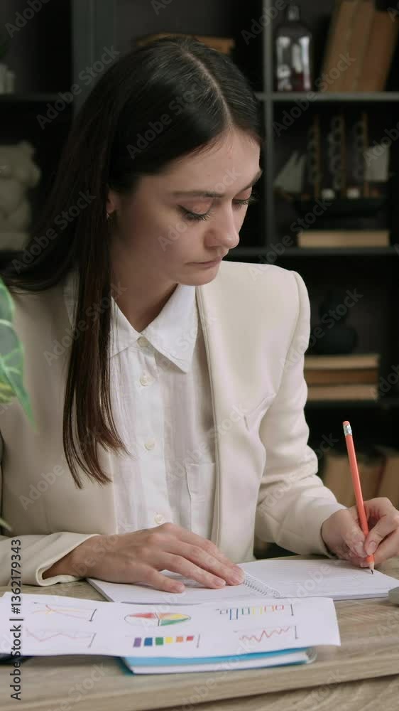 Student intern in classic suit sitting at an office table. Woman analyzing several company statistics and charts and thinking about creating several growth strategies. Business development company. Student intern in classic suit sitting at an office table. Woman analyzing several company statistics and charts and thinking about creating several growth strategies. Business development company.