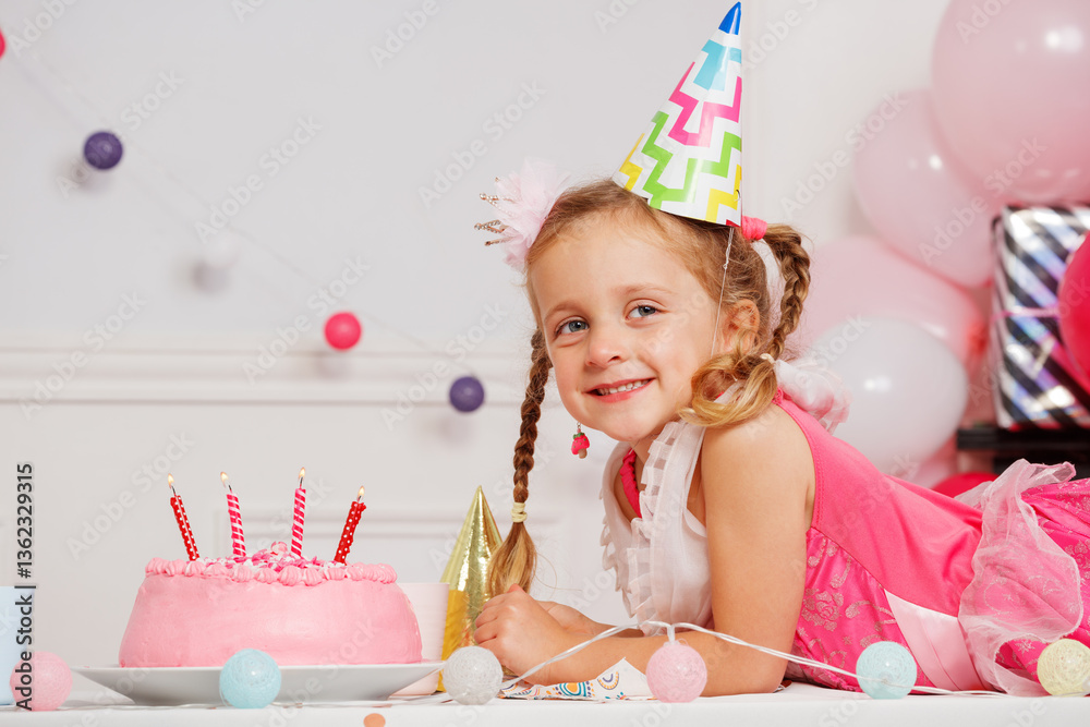 Girl with hat smiles at cake during a colorful birthday party