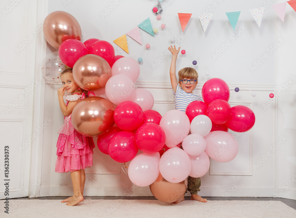 Two kids boy, girl, hiding in vibrant balloons at birthday party