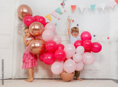 Obraz na płótnie Two kids boy, girl, hiding in vibrant balloons at birthday party w salonie