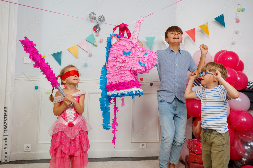 Child in a blindfold and dress aiming stick at unicorn pinata