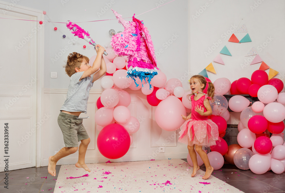 Excited boy in a jump hitting unicorn pinata at birthday party