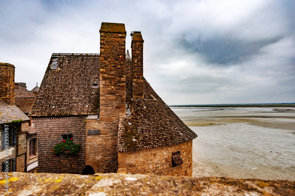 Old stone castle wall of Mont Saint Michel beside sandy shore
