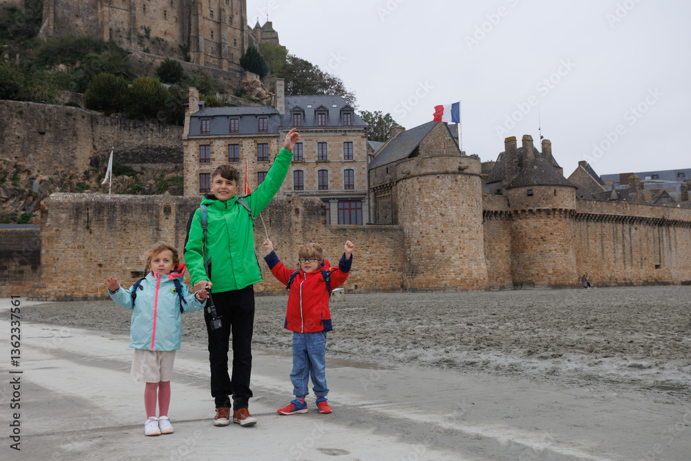 Three kids pose excitedly near historic stone Mont Saint Michel