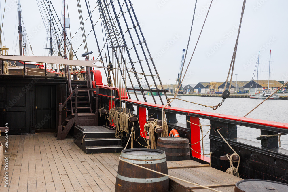 Historic sailing ship docked with barrels and ropes on the deck