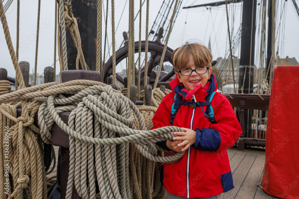 Child in red coat on ship, smiling and holding rope during visit