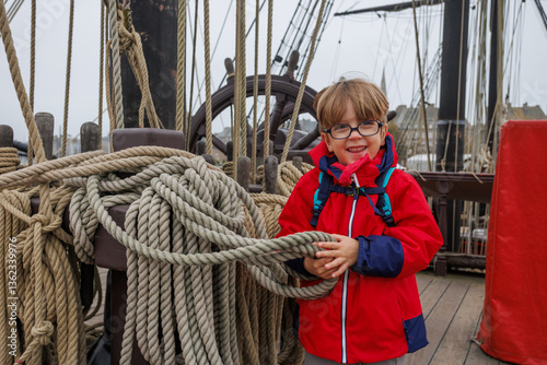 Obraz na płótnie Child in red coat on ship, smiling and holding rope during visit w salonie