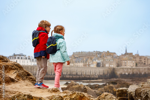 Obraz na płótnie Two kids explore rocky coast with port town view in the distance w salonie