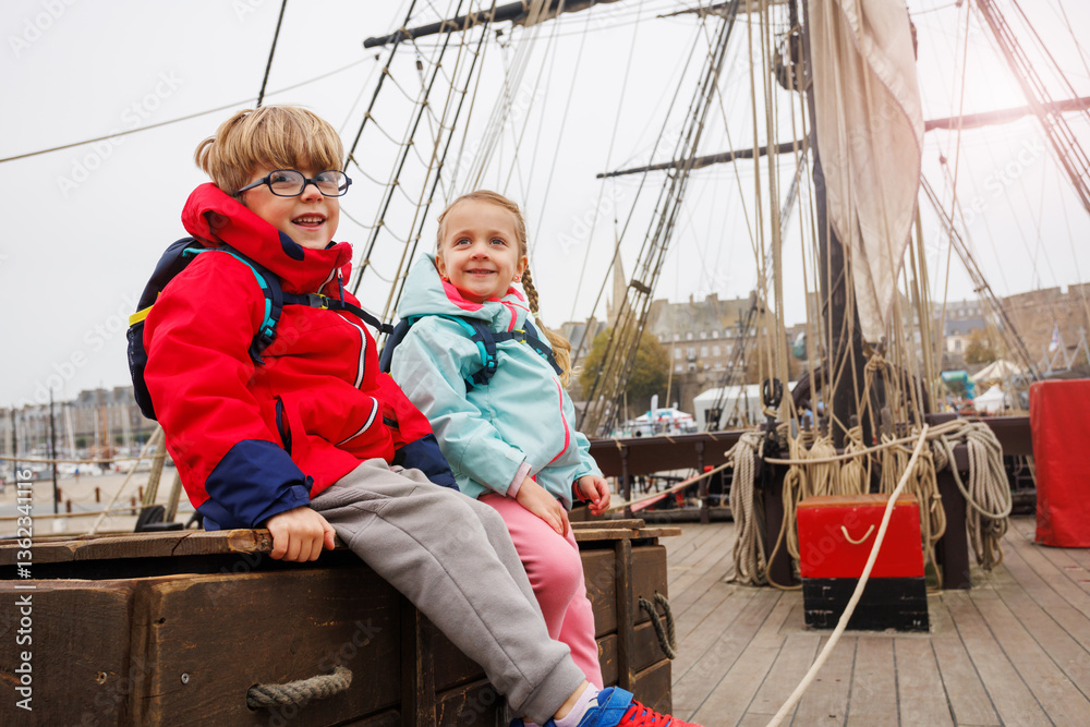 Kids travelers enjoy sitting on a ship, smiling under cloudy sky