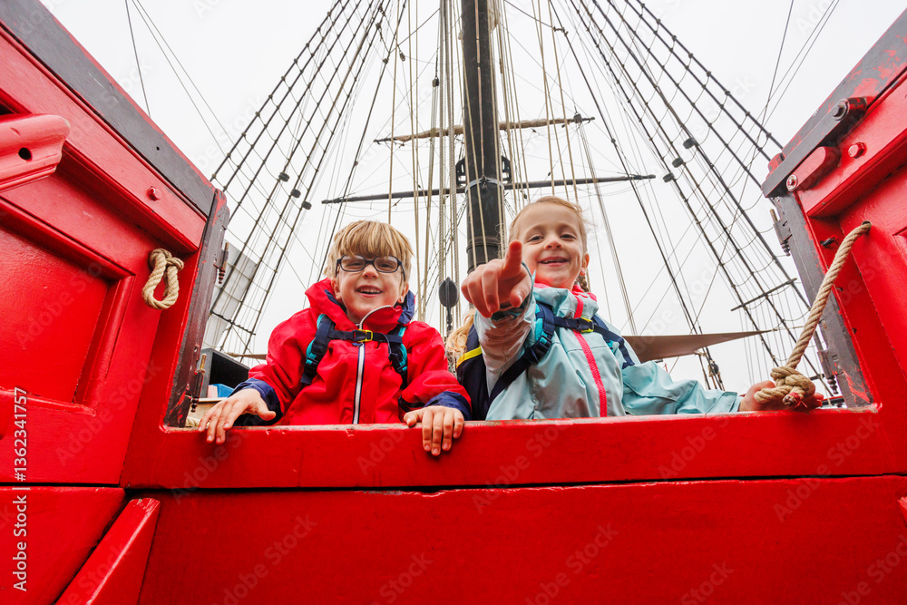 Excited children tourists aboard red ship, pointing and laughing