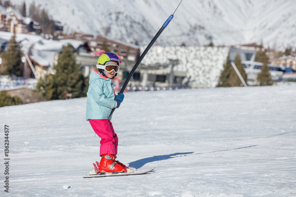 Little skier in snowy day on ski lift with colorful hat and gear