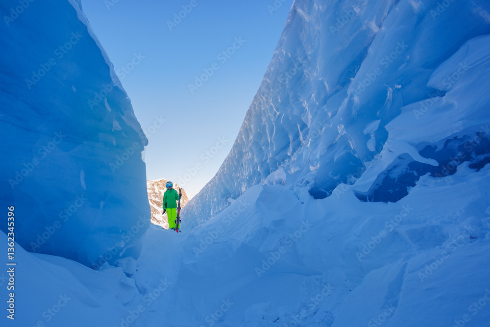A vibrant skier boy stand on snowy path flanked by icy cliffs