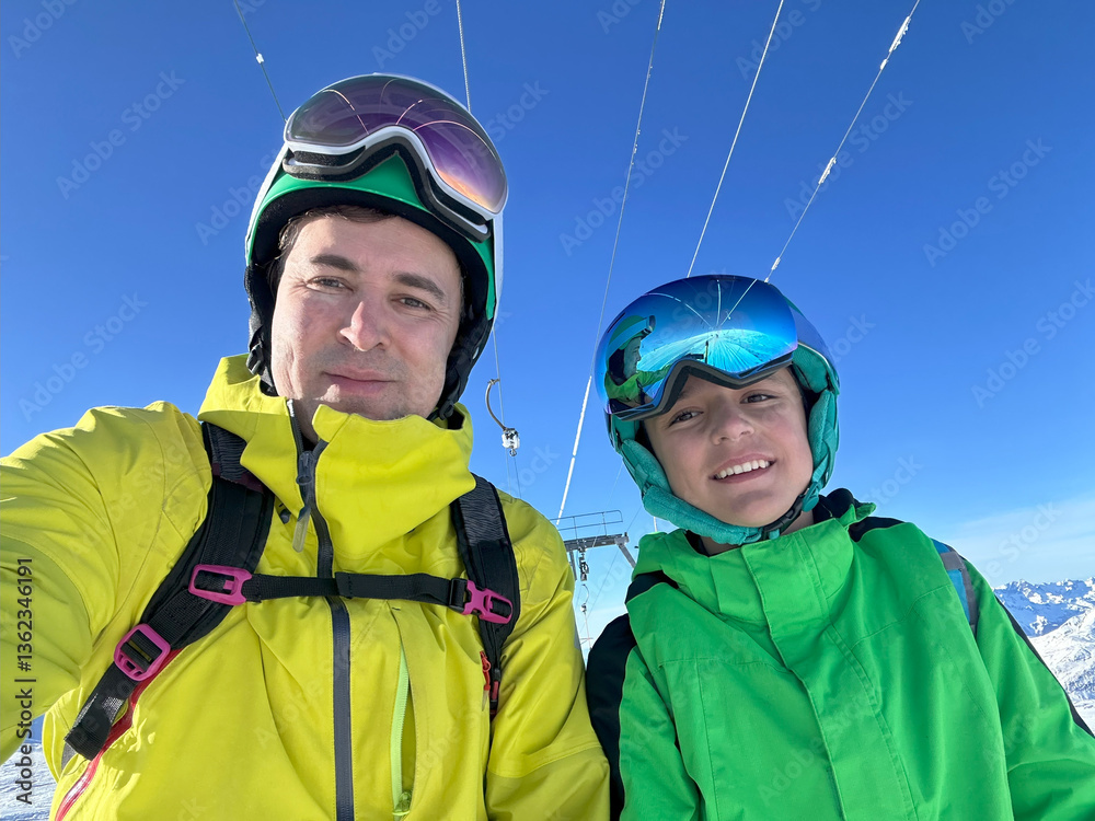 Skiers dad and son enjoy sunny day on slopes in colorful gear