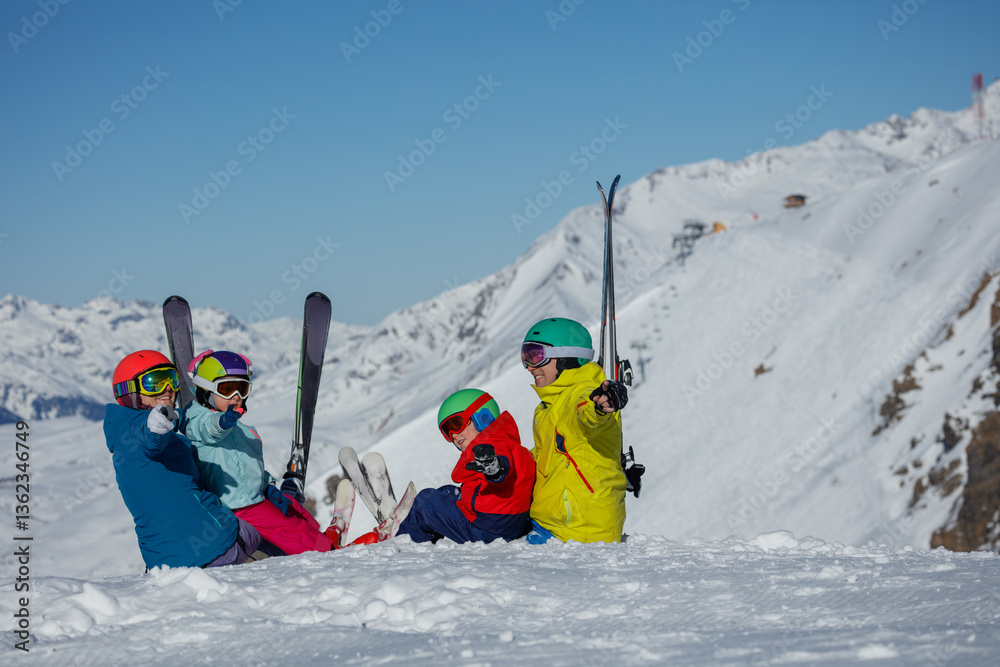 Family in helmets sits on snow, skiers enjoying alpine scenery