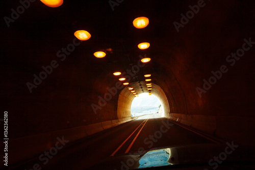 Two lane highway through a tunnel, view of the lights leading to the daylight and the end of the tunnel.
