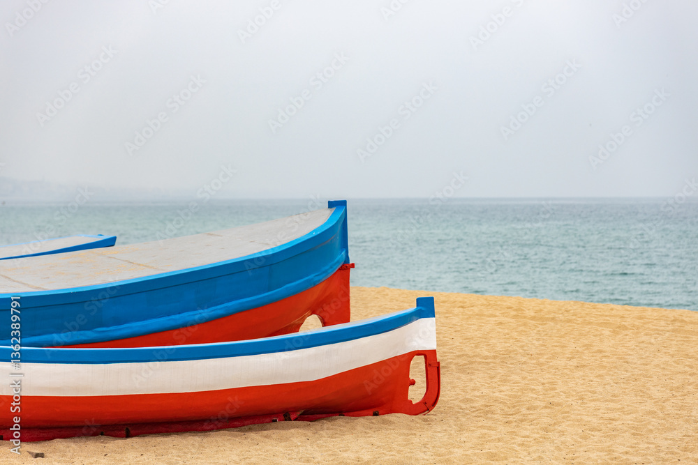 Fototapeta premium Two boats are sitting on the beach, one blue and one red