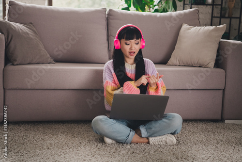 Young woman enjoying comfort at home sitting on carpet with laptop and headphones during a relaxed and leisure weekend