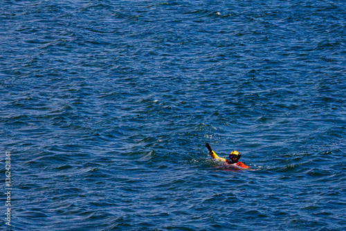 US Coast Guard helicopter demo rescue with rescue swimmer in the water with a raised hand.