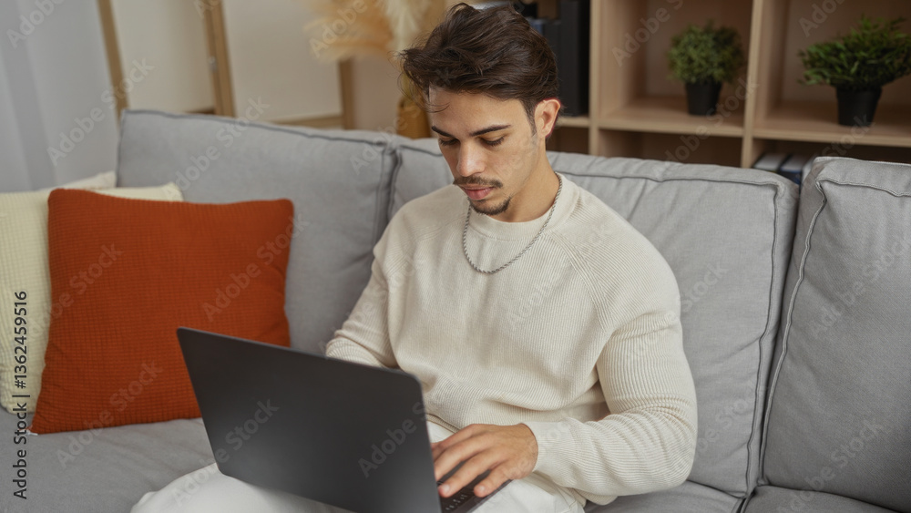 Young hispanic man using laptop on a comfortable sofa in a cozy living room showcasing modern interior design and relaxed home atmosphere Young hispanic man using laptop on a comfortable sofa in a cozy living room showcasing modern interior design and relaxed home atmosphere
