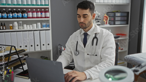 Wallpaper Mural Young hispanic man in hospital workplace working indoors in clinic while using laptop surrounded by medicine bottles. Torontodigital.ca