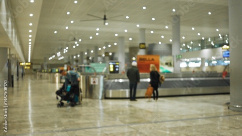 Blurred travelers with luggage waiting at an airport baggage claim indoors with bright overhead lighting and spacious terminal design