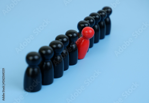 Talents and skills concept. Red colored figure in row of black wooden people figures on blue background.