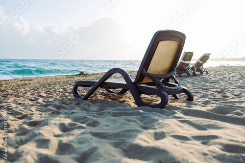 Fototapeta Naklejka Na Ścianę i Meble -  A sandy beach with cozy sun loungers facing the sea, against the backdrop of soft sunlight. An atmosphere of coziness, silence and complete relaxation. Mediterranean Sea, Turkey