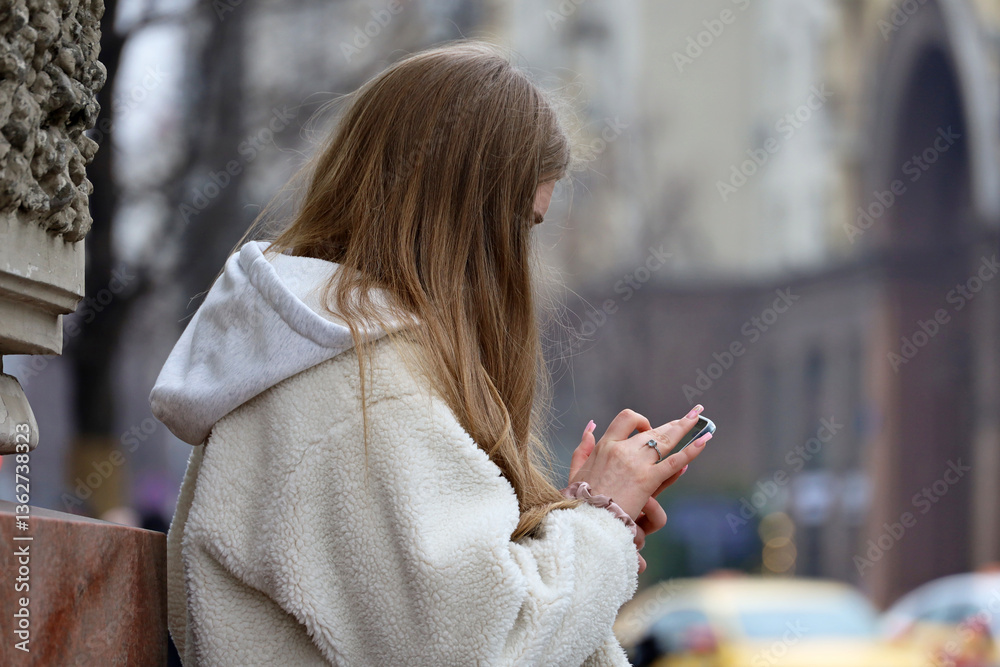 Young woman using mobile phone on city street at spring, smartphone in female hands with manicure
