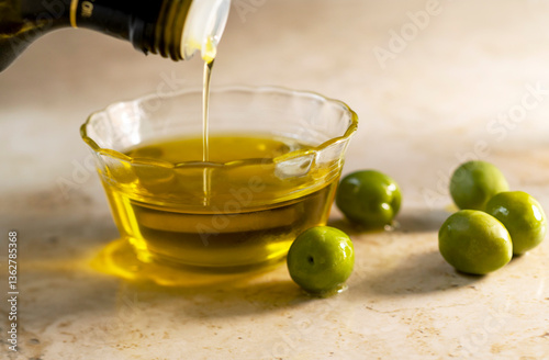 Olive oil pouring into small glass bowl with olives on table