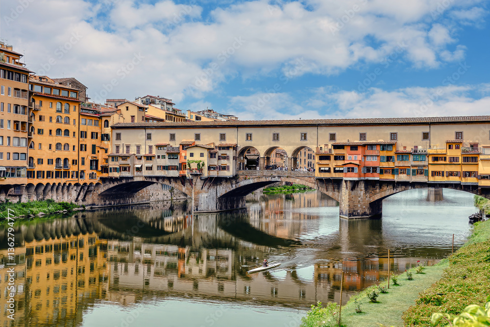Obraz premium The Ponte Vecchio bridge in Florence showcases its colorful buildings and shops reflecting in the tranquil waters Arno river.
