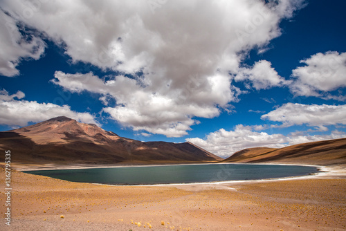 Puffy clouds over lake and barren mountains in Atacama Desert