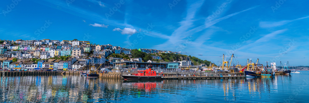 Obraz premium Brixham Devon panoramic view harbour fish market and houses on hillside with blue sea and sky UK