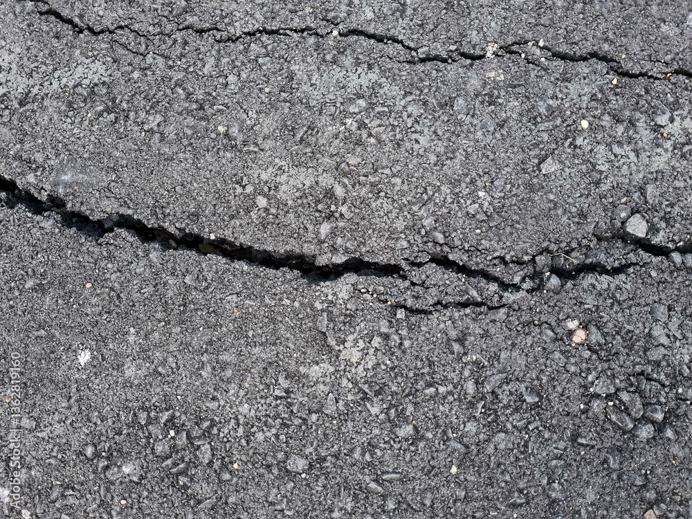 Obraz premium Cracked asphalt road surface background. Surface texture of new asphalt road with cracks. Alligator type cracking in the asphalt pavement. Cracks on asphalt in a afternoon day.