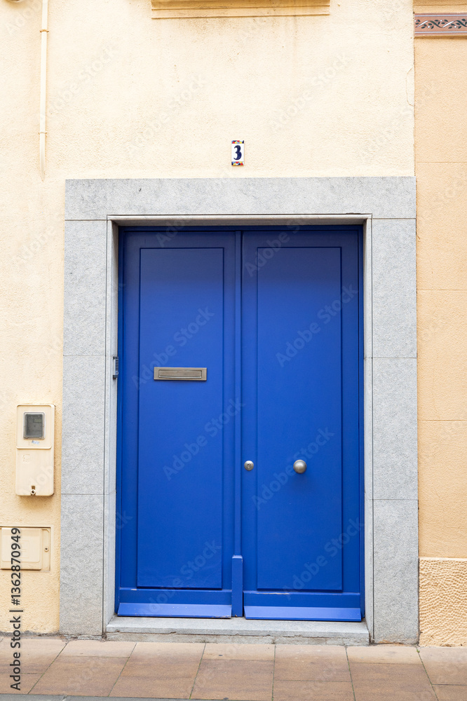 Fototapeta premium Vibrant blue door with silver frame on beige wall and sidewalk