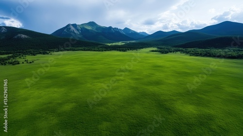 Expansive green meadow nestled amidst towering mountains.  Vast grassy plain stretches out beneath a partly cloudy sky, framed by a backdrop of rugged peaks