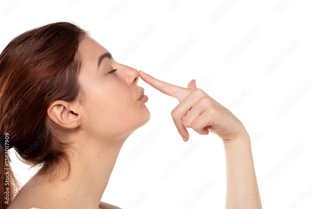 Young woman with long brown hair touching her nose, suggesting nose job or rhinoplasty. Profile view, white background Young woman with long brown hair touching her nose, suggesting nose job or rhinoplasty. Profile view, white background
