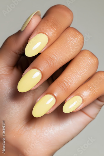 Woman's hand with elegant pastel yellow almond-shaped manicured nails, showcasing nail art, beauty trends, and salon services.