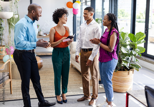 Diverse colleagues in office celebrating success, smiling and holding congratulatory card