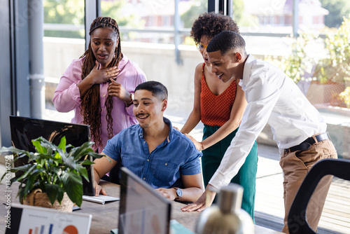 Diverse team collaborating around computer, discussing project in modern office